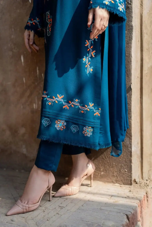 Blue embroidered outfit with floral patterns worn by a person, standing against a textured wall.