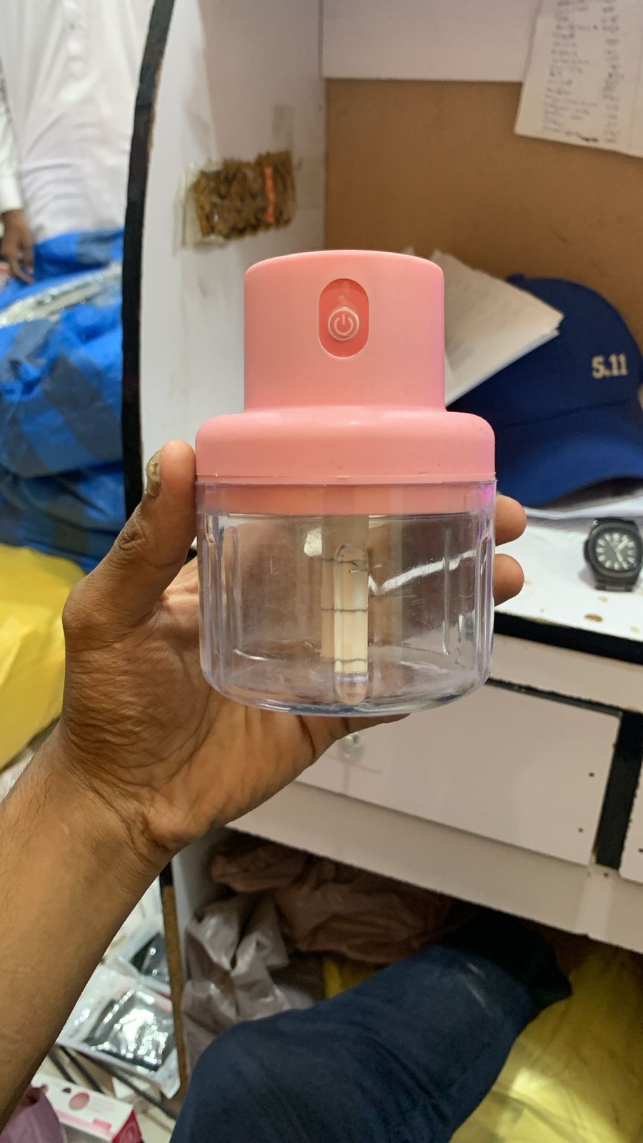 Hand holding a pink and clear kitchen tool against a cluttered background